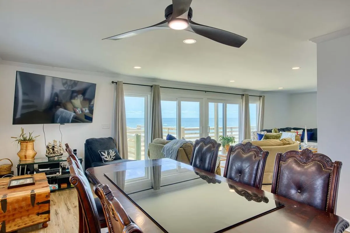 The spacious interior features a large dining table, floor-to-ceiling windows, a comfortable seating area, and a TV. The openness and organization reflect a welcoming, practical space likely adjacent to the main entry, connecting to storage and other key amenities.