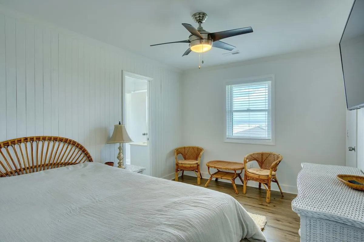 A tranquil living space with a rattan bed, ceiling fan, window letting in natural light, rattan chairs, and a television. The area looks cozy and social—ideal for movie nights or relaxed gatherings.