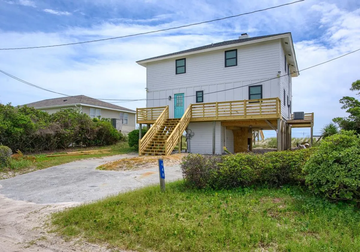 This exterior image showcases the two-story house's green entry door, a wooden deck, and ample surrounding greenery. The scene implies an accessible entry point for guests, with space in front likely accommodating multiple vehicles, which supports the parking feature.